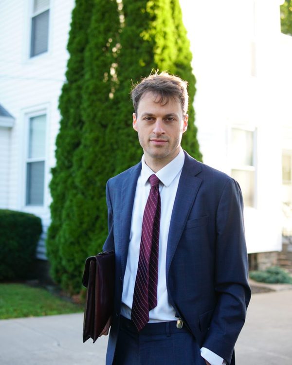 Thomas Plan in a navy suit in front of a white house.